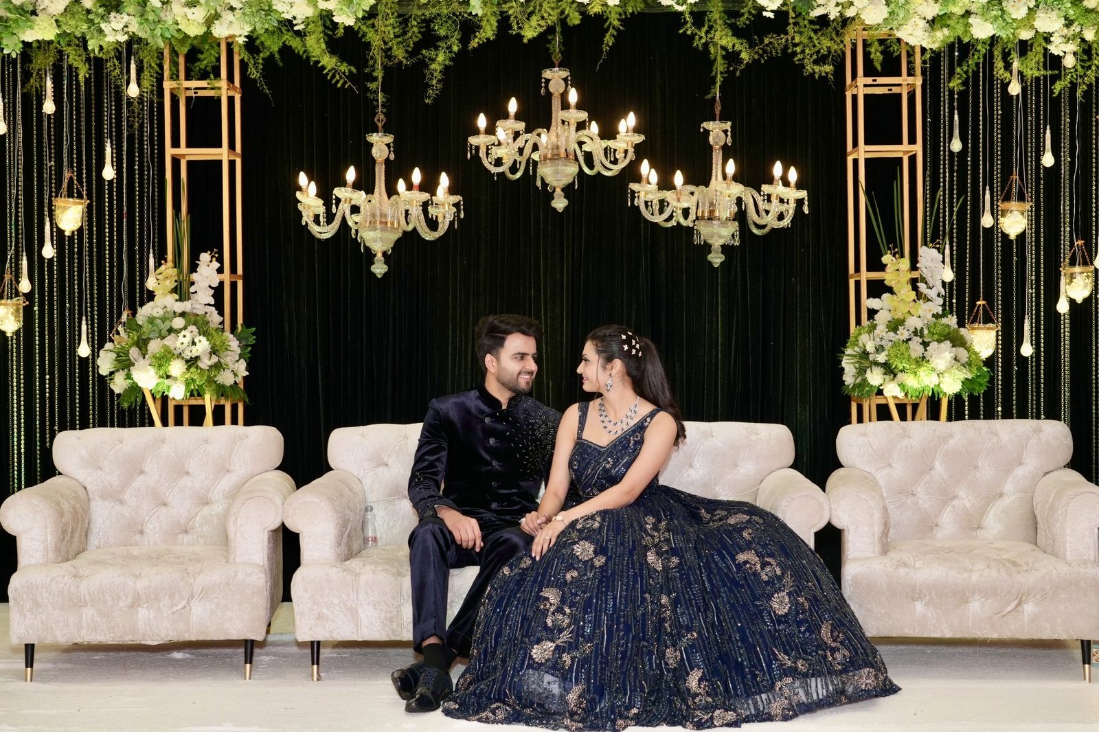 Couple seated at an elegant reception stage with chandeliers