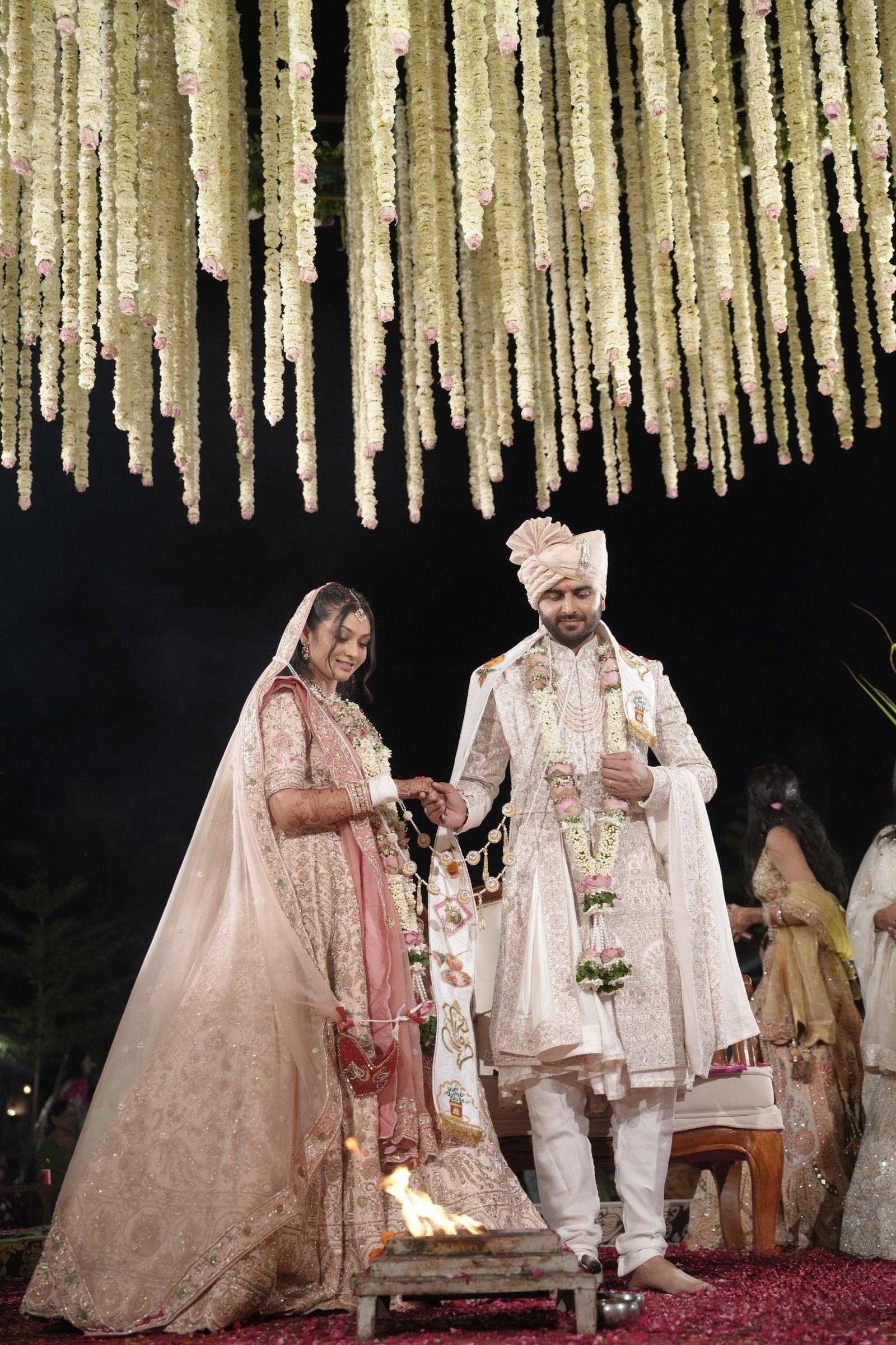 A couple takes their pheras beneath a canopy of hanging garlands